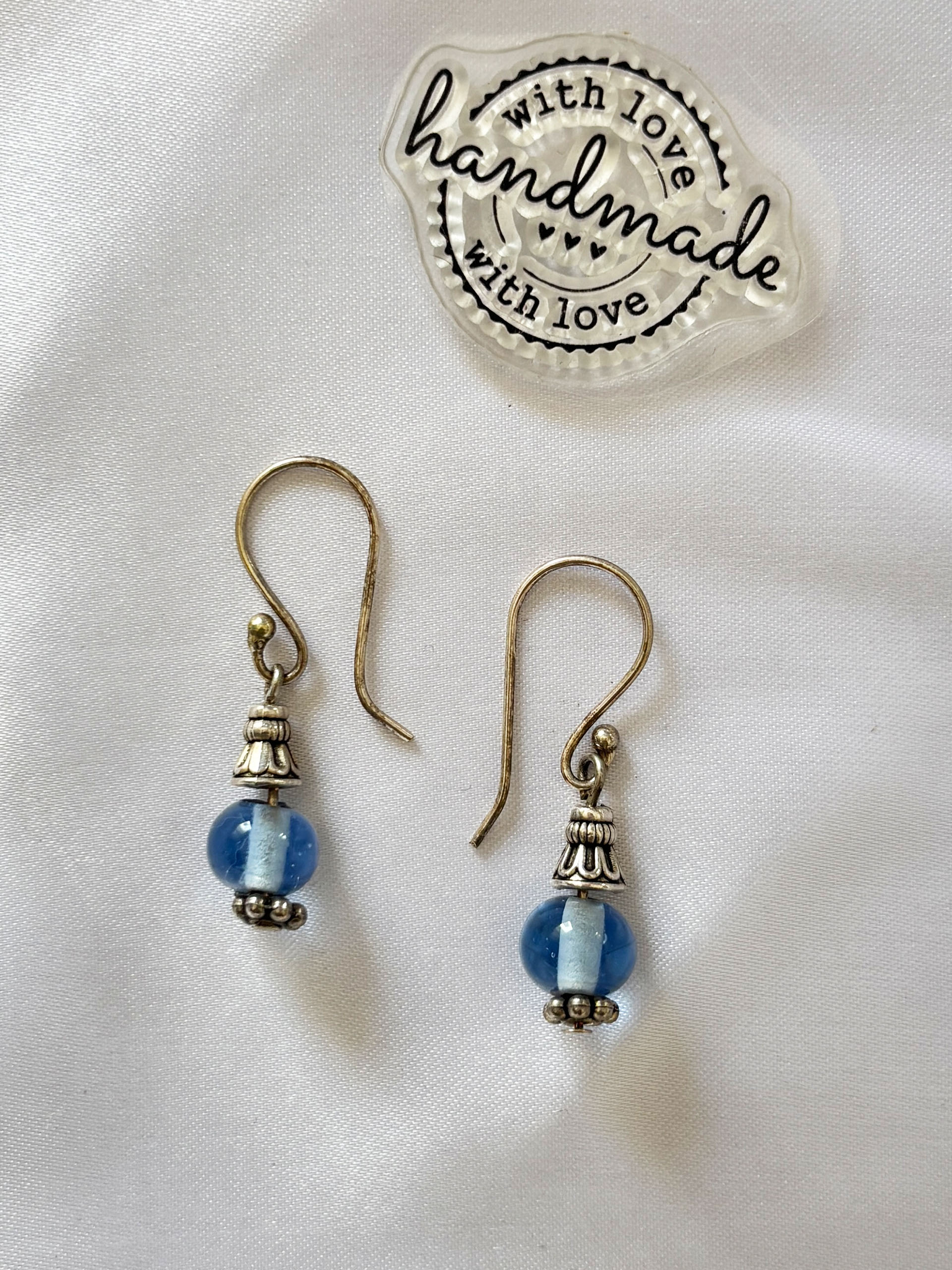 Azure Charm Earrings - These beautifully crafted earrings feature soft blue glass beads paired with antique silver accents, creating a look that is both classic and graceful. The subtle shimmer of the bead combined with the intricate detailing adds a refined touch without being too bold.