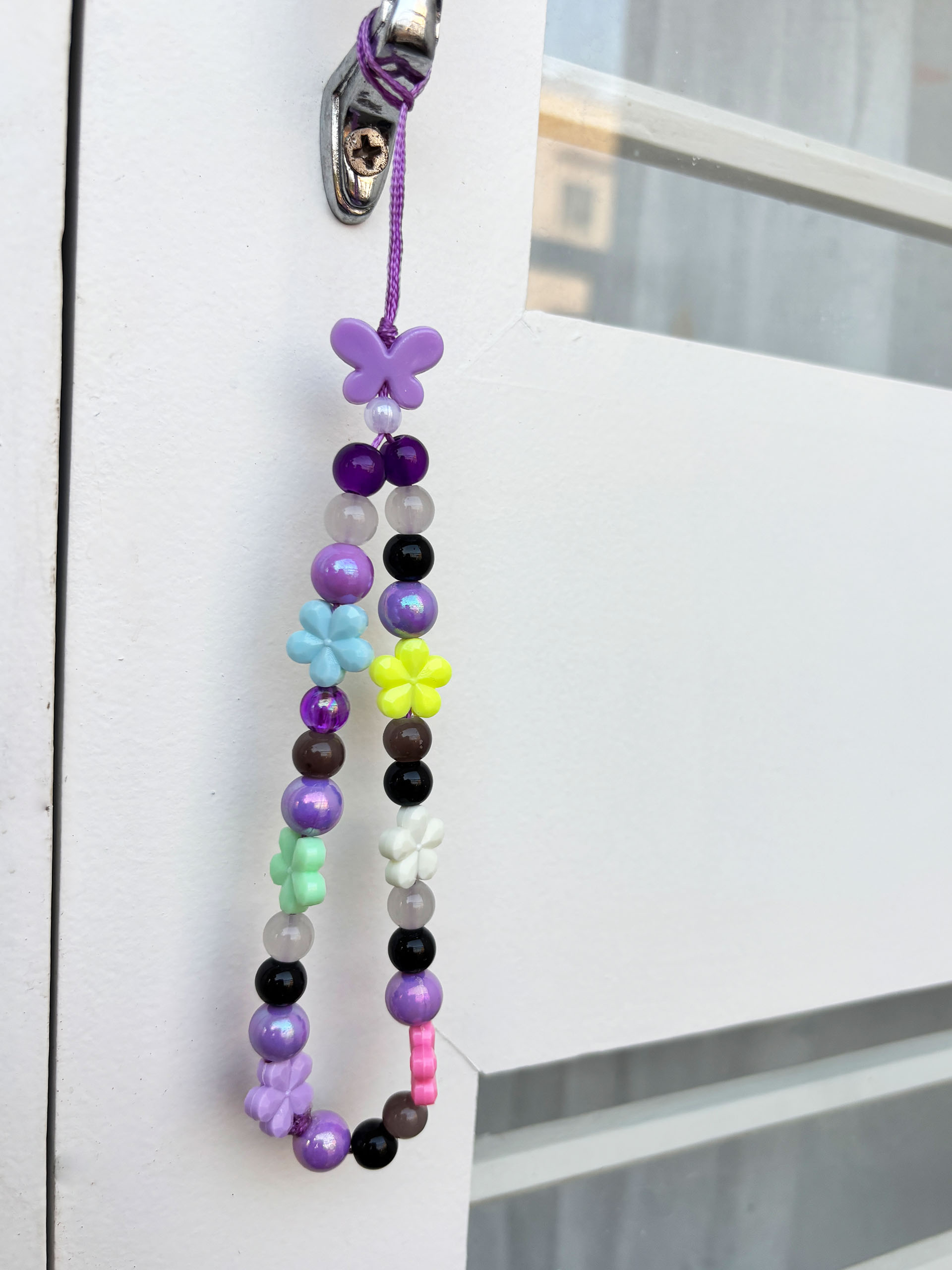 Purple Candy Bloom Beaded Charm - Bright, fun, and full of personality, this beaded charm strap is designed to stand out. Featuring a vibrant mix of glossy beads and cute flower accents, it brings together a cheerful blend of purples, pastels, and pops of bold color.