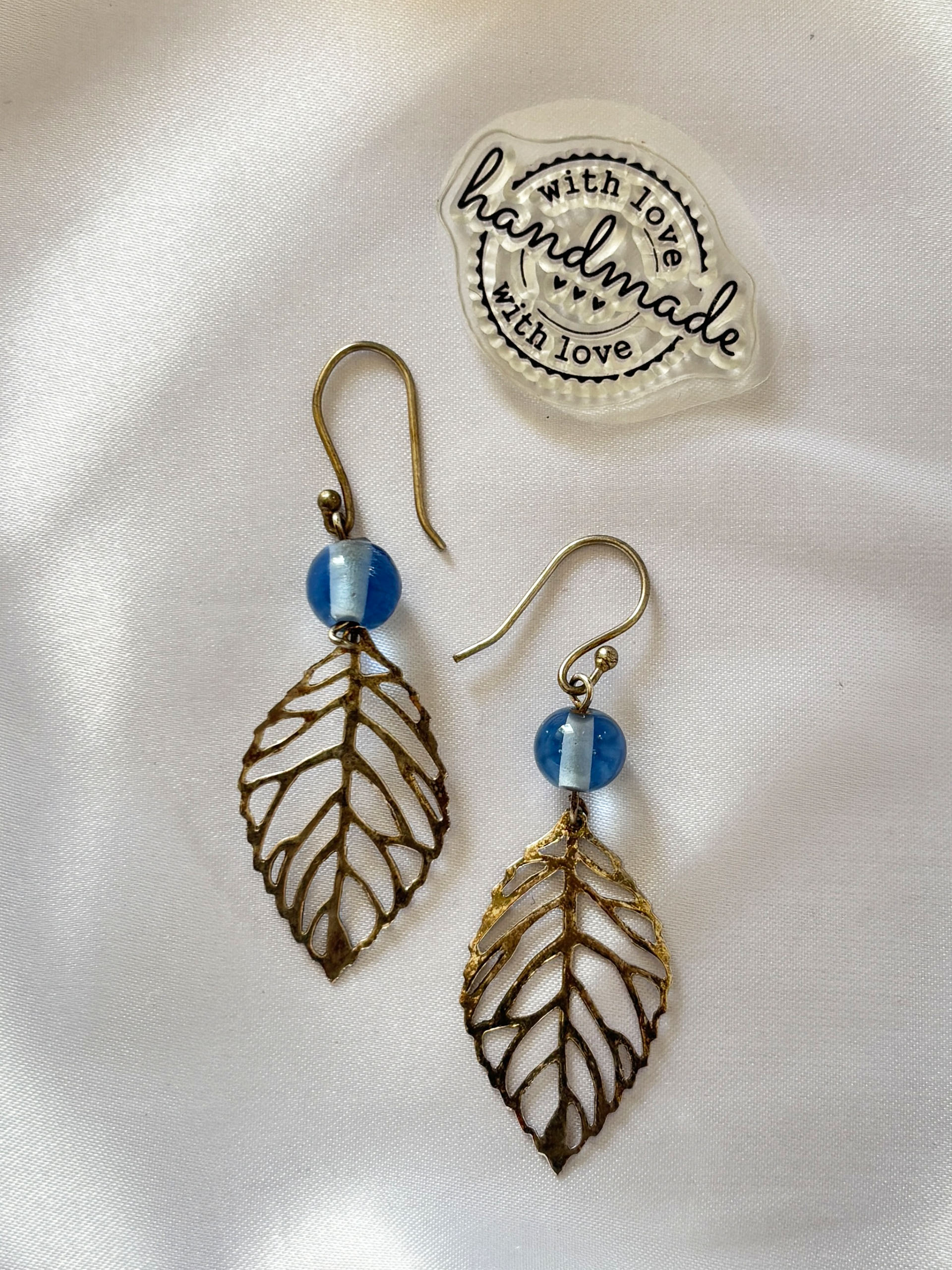 Minimal Leaf Dangle Earrings - These statement earrings feature delicate gold-toned leaf charms paired with soft blue beads, creating a perfect blend of nature-inspired design and subtle colour.